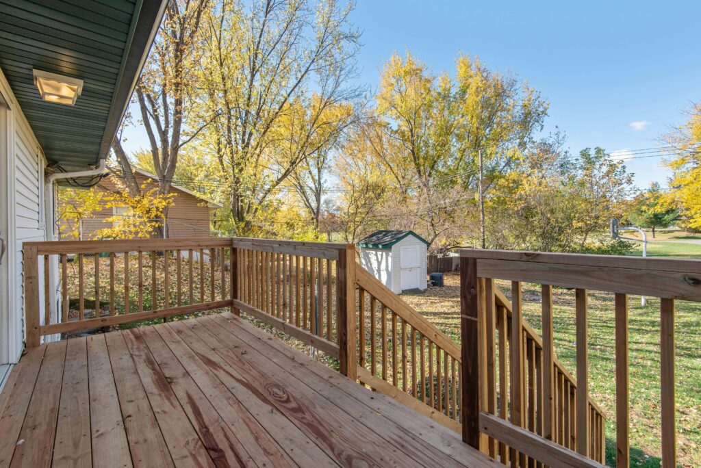 Wooden backyard deck with railing and stairs overlooking a residential yard with trees and a small shed